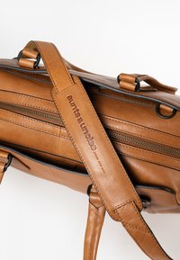 Bruine leren tas met een gestructureerd ontwerp, voorzien van twee ritsen, een afneembare schouderband en een reliëflogo op de band.