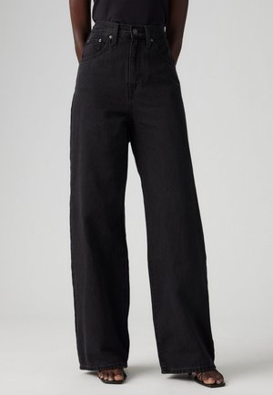 Høytliv, vide svarte jeans i denimbomull. Har frontlommer, metallknapplukking og subtil kontrastsøm.
