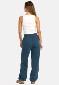 Lätta, mörk teal joggers med elastisk midja, lös passform och kontrasterande sömmar, kombinerade med en vit linne.