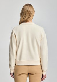 Felpa color crema con una vestibilità ampia, polsini e orlo a costine, caratterizzata da una texture morbida e un collo tondo.