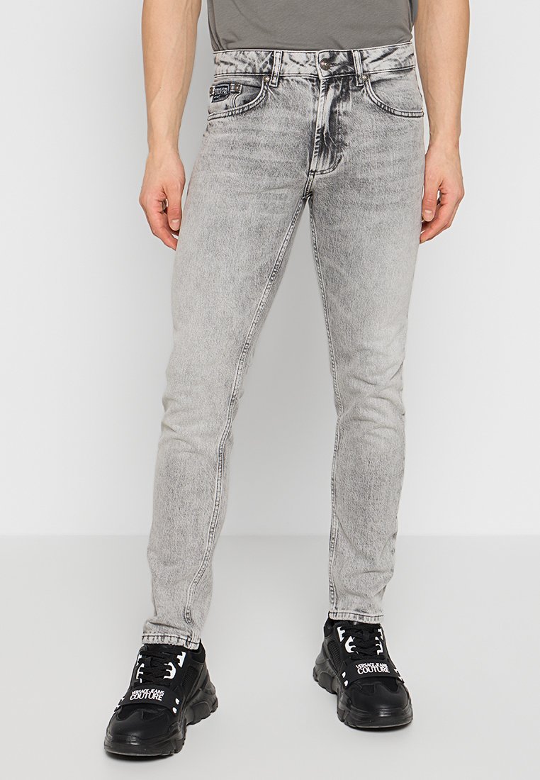 Jeans skinny grigi sbiaditi con un aspetto rovinato, design a cinque tasche e chiusura a bottone, abbinati a sneakers nere.