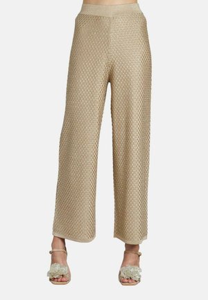 Pantaloni a gamba larga in tessuto dorato abbinati a tacchi aperti dorati con grandi decorazioni floreali.