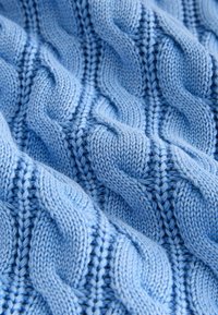 Tissu tricoté doux bleu clair avec un motif épais en relief de mailles torsadées créant un design texturé de corde tordue.