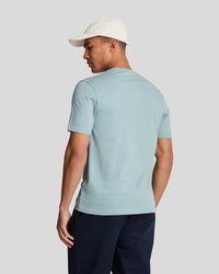 T-shirt en coton bleu clair à manches courtes, avec un col rond et une coupe décontractée. Porté avec un pantalon bleu marine et une casquette blanche.