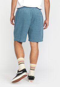 Lichtblauwe corduroy shorts met een elastische tailleband, een enkele achterzak en opgerolde zomen, gestyled met beige en gestreepte sokken.