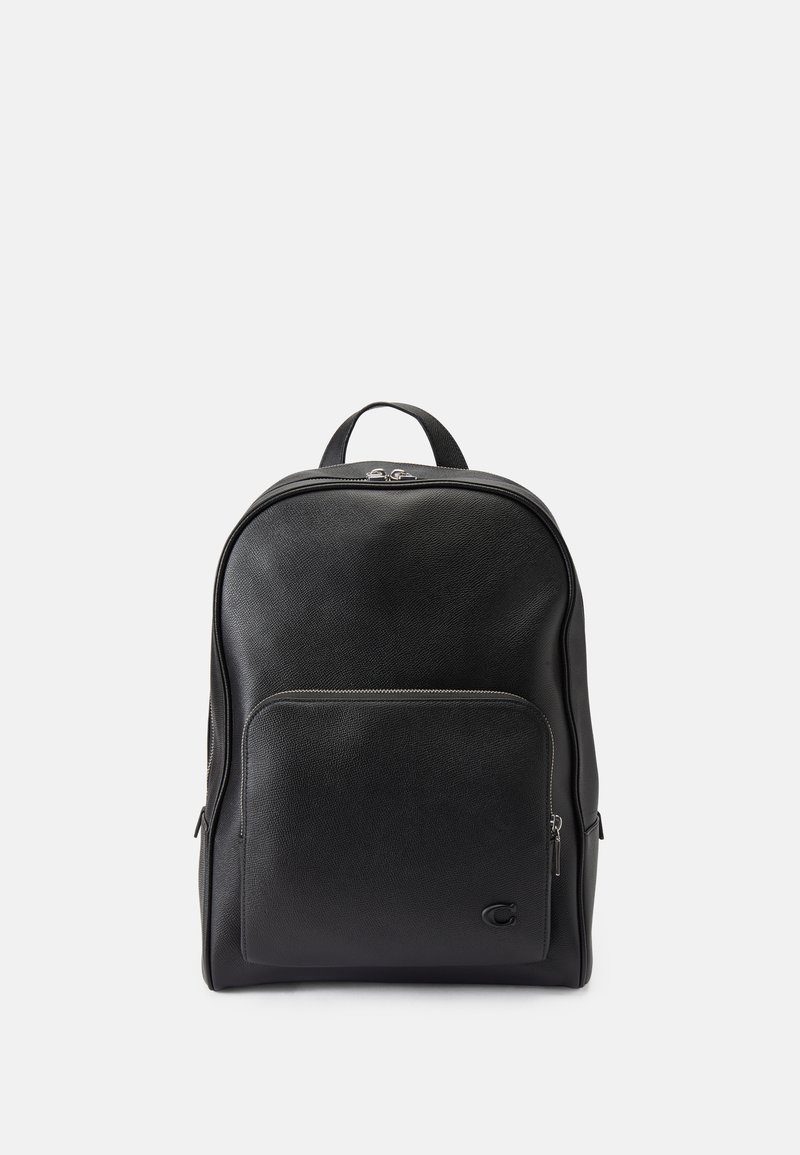 Mochila preta de couro com uma textura suave, forma arredondada, bolso frontal com fecho éclair e uma alça superior. Apresenta uma marcação discreta na lateral.