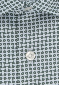 Camicia di stoffa azzurro chiaro con un motivo geometrico verde e bianco, caratterizzata da un bottone bianco davanti, texture liscia e senza loghi visibili.