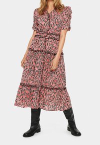 Květinové maxi šaty v růžové a černé barvě s balónovými rukávy, volánkovými vrstvami a úzkým pasem. V kombinaci s černými kozačkami po kolena.