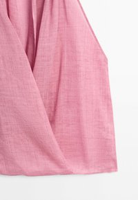 Roze mouwloze linnen jurk met een wikkelstijl aan de voorkant en getextureerd stofdetail, getoond op een witte achtergrond.