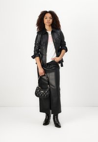 Giacca di pelle nera con maniche arrotolate, t-shirt bianca con grafica, gonna di pelle nera, borsa nera trapuntata, e stivaletti neri.