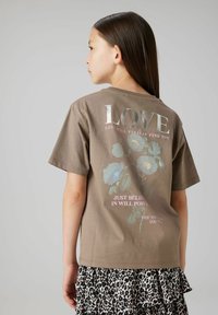 Brun bomull T-shirt med blommönster och text på baksidan. Kort ärm, avslappnad passform. Bärs med en kjol i svart och vit leopardtryck.
