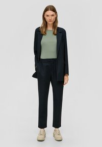 Marineblauwe pinstripe blazer met bijpassende broek, gecombineerd met een aansluitend groen topje. De outfit heeft een ontspannen ontwerp en neutrale sneakers.