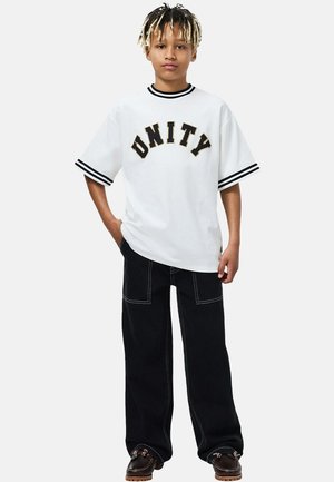 Wit shirt met korte mouwen en zwarte accenten, met "UNITY" in vette letters. Zwarte broek met wijde pijpen, contrasterende stiksels en zakken.
