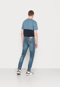 T-shirt em algodão para homem com combinação de cores em azul claro e azul marinho, combinado com jeans skinny azul desbotado e ténis brancos com detalhes em dourado.
