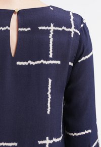 Laivaston sininen pusero, jossa on avainreikäselkä, valkoisella abstraktille kuviolle, pehmeä kangas ja pyöreä kaula-aukko.