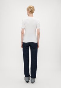 Camiseta blanca de manga corta con escote redondo, combinada con jeans rectos de color azul oscuro; los jeans tienen un detalle de puño doblado en contraste.