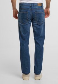 Donkerblauwe denim jeans met een rechte pasvorm, voorzien van twee achterzakken en een merknaam in een leren bruine patch op de tailleband.