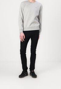 Sudadera gris claro con cuello redondo y puños acanalados, combinada con jeans ajustados negros y zapatillas negras.