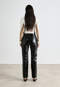 Pantalons en cuir synthétique noir avec une finition brillante, taille haute et jambes droites. Haut à manches longues en crème avec des accents beiges sur les manches.