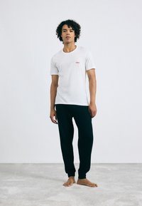T-shirt en coton blanc avec un logo "HUGO" rouge, associé à un pantalon de jogging noir. Le t-shirt a des manches courtes et un col rond.
