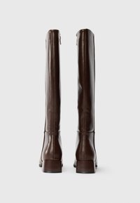 Ein Paar hohe, dunkelbraune Lederstiefel mit Blockabsätzen, von hinten vor einem schlichten weißen Hintergrund betrachtet.