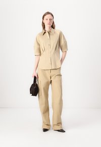 Beige button-up shirt with short, structured sleeves paired with matching wide-leg trousers. Accessorized with a small black bag.