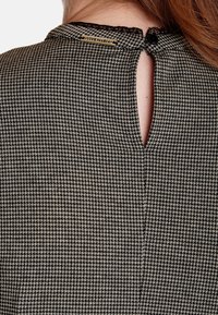 Svart och vit mönstrad tygklänning med nyckelhålsöppning i ryggen, spetsdetaljer och en liten guldlapp som säger "Vive Maria" fäst vid halsringningen.