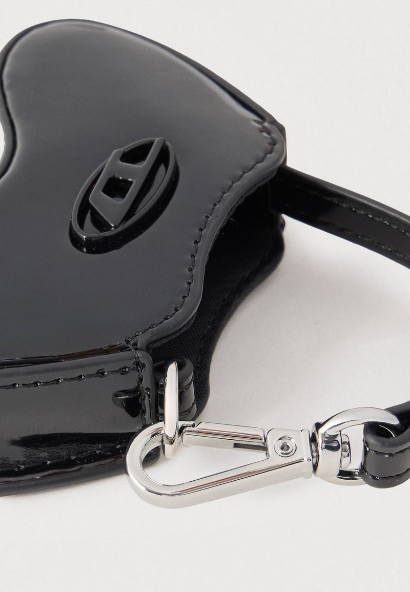 Accesorio en forma de corazón de charol negro con una hebilla central y un broche de metal plateado unido a una correa negra.