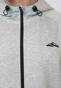 Φούτερ με φερμουάρ ανοιχτό χρώμα γκρι, με μαύρο λογότυπο βουνού στο στήθος και μαύρα ρυθμιζόμενα κορδόνια στο κουκούλι.