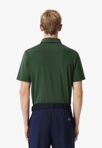 Mörkgrön kortärmad polo med klassisk krage. Tyget är slätt, matchat med marinblå byxor och ett kontrasterande bälte.