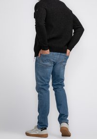 Mörk stickad tröja, ljusblå denimjeans och grå sneakers. Jeans med bakfickor och en avslappnad passform. Avslappnad outfit sedd bakifrån.