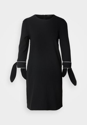 Robe noire à manches longues, comportant des détails bouffants et des accents à nouer aux poignets. Design simple et texture lisse. Fermeture éclair au dos.