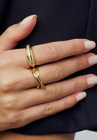 Tre guld ringe bæres på en hånd. Den ene har et glat bånd, den anden har et indviklet mønster, og den tredje har et snoet design.