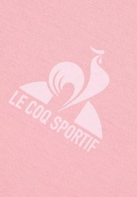 Tessuto di cotone rosa chiaro con un logo stampato bianco di "Le Coq Sportif" caratterizzato da elementi di design stilizzati.