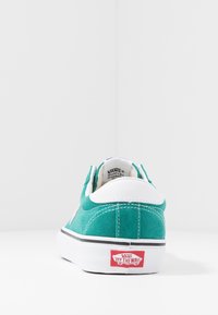 Teal Vans-sneaker med vit häldel, vit sula och röd "Vans Off The Wall"-logotyp på baksidan, visad från bakre utsikt.