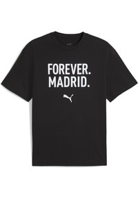 Melna kokvilnas T-kreklu ar īsām piedurknēm, uz kura redzams liels balts teksts: "MŪŽĪGI. MADRID." Zem teksta atrodas mazs balts Puma logo.