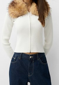 Vit randig zip-up tröja med en krage av konstpäls i beige, i kombination med mörkblå högmidjade jeans. Slim fit och texturerad tyg.