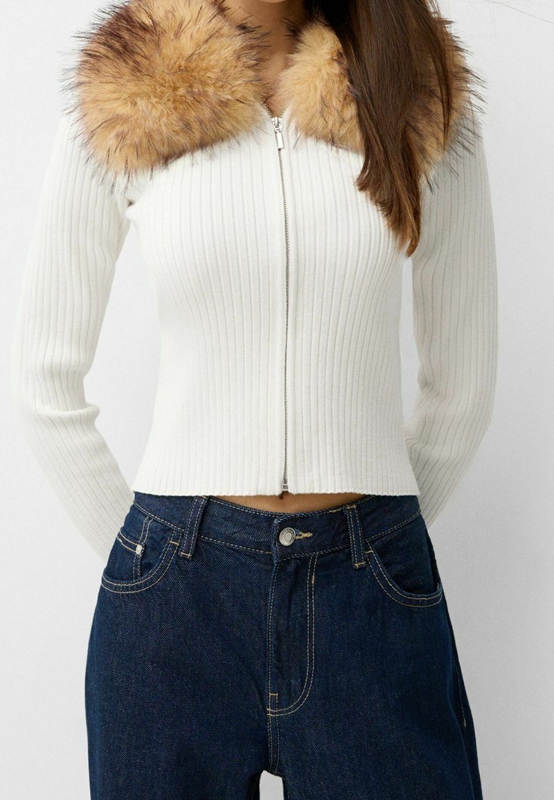 Vit randig zip-up tröja med en krage av konstpäls i beige, i kombination med mörkblå högmidjade jeans. Slim fit och texturerad tyg.