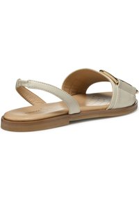 Sandalia de cuero crema con correa ajustable, suela plana, diseño minimalista y un acento en tono dorado en la parte superior.