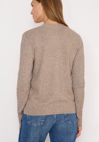 Beige stickad tröja med rund halsringning, ribbat fåll och kabelstickning längs ärmarna. Bärs med blå jeans.