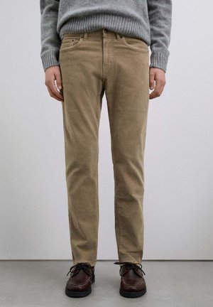 Pantalones de pana beige con diseño de pierna recta, que cuentan con bolsillos frontales y un frente plano, combinados con zapatos de cordones marrón oscuro.