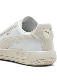Puma sneaker, fehér bőr felsőrésszel, bézs velúr díszítéssel, arany logó részletezéssel és texturált gumitalppal.