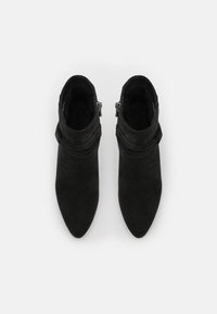 Bottines noires en cuir suédé avec un bout pointu et un détail froncé autour de la cheville, dotées d'une fermeture éclair sur le côté.