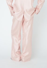 Light pink satin suit featuring wide-leg trousers and a fitted jacket with silver button details, showcasing a smooth texture and sophisticated design.