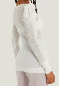 White knit sweater featuring a textured pattern, puffed sleeves, and ribbed cuffs. Designed with a form-fitting silhouette.