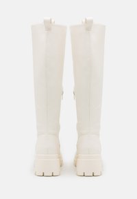 Bottes blanches jusqu'au genou en matériau synthétique lisse, avec une semelle épaisse, des zips latéraux doubles et des accents en boucle à l'arrière.