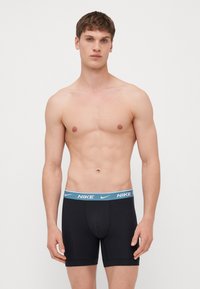 Sorte boxer briefs med en lys blå Nike-logo i taljen. Stoffet ser glat ud med et tætsiddende design, ingen synlige mønstre eller detaljer.
