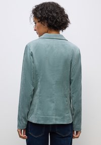 Vaaleansininen samettimekkopuku, jossa on leikkauskaulus ja pitkät hihat. Tekstuuri on pehmeä pystyripustuksilla, ja siinä on istuva malli sekä hienovarainen kiilto.