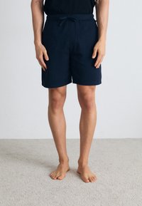 Pantalones cortos de color azul marino, hechos de una tela suave, con una cinturilla elástica y cordón ajustable, de corte recto y que terminan por encima de la rodilla.