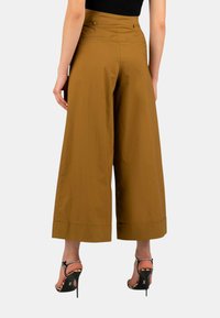 Pantaloni larghi marroni realizzati in tessuto leggero, caratterizzati da una vita alta, tasche laterali e una finitura pulita all'orlo.